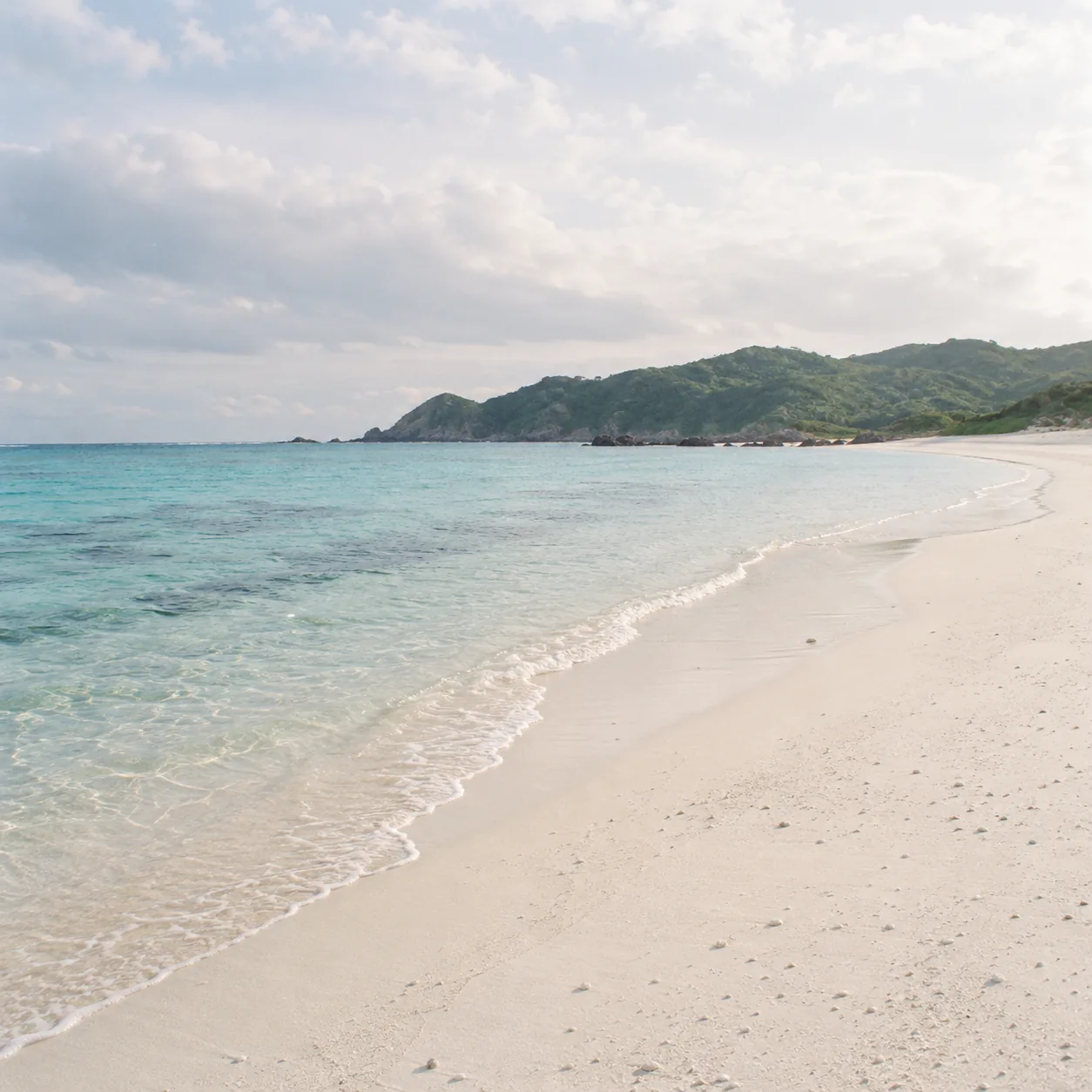 朝の白い砂浜と、うすい水色の浅瀬